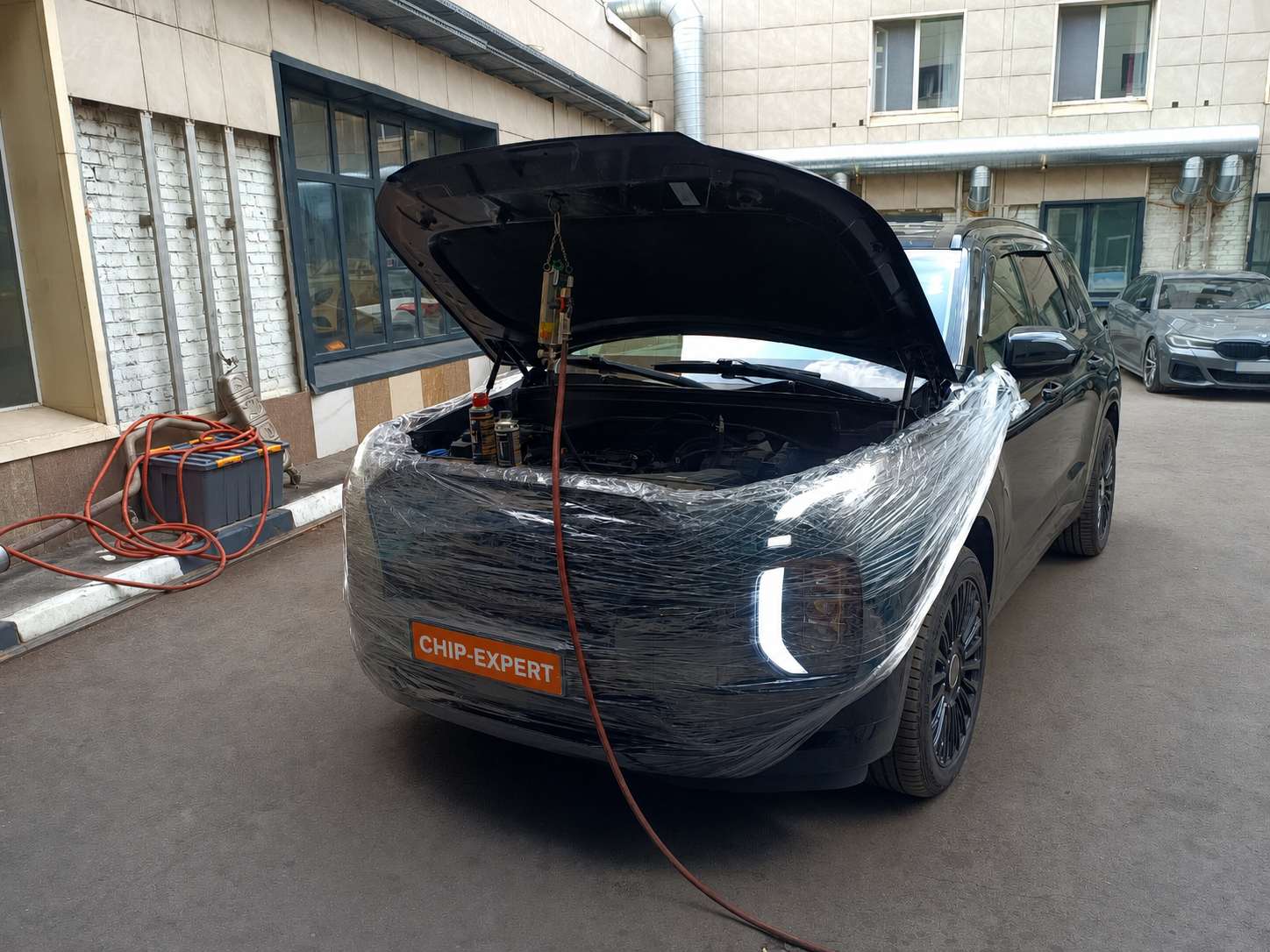 Hyundai Palisade 2.2D 2019, вид спереди справа, с открытым капотом и защищённой плёнкой передней частью во время работ с сервисным оборудованием в мастерской Чип-Эксперт — chip-expert.pro.