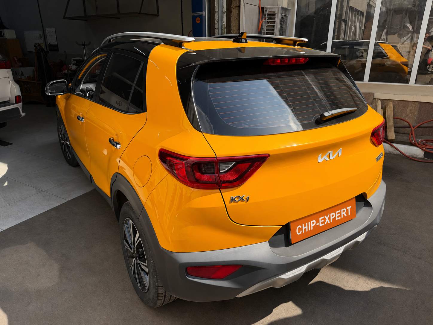 Жёлтый Kia KX1 (QE) 1.4 2022, вид сзади слева в ремонтной зоне мастерской Чип-Эксперт — chip-expert.pro.
