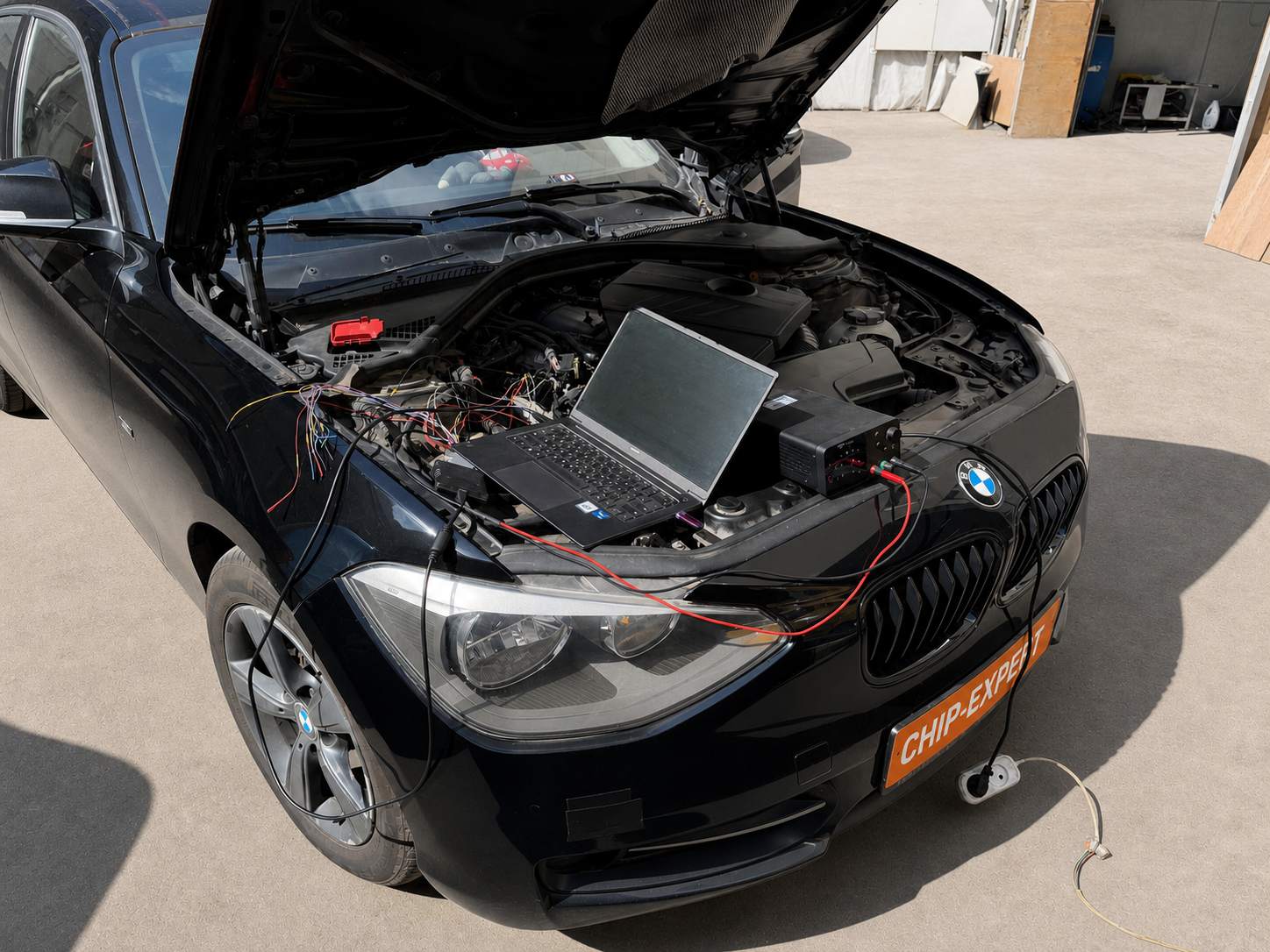 BMW 1 Series 118i 2012 с открытым капотом во время программирования ЭБУ с помощью ноутбука, программатора и проводов прямого подключения в мастерской Чип-Эксперт — chip-expert.pro.