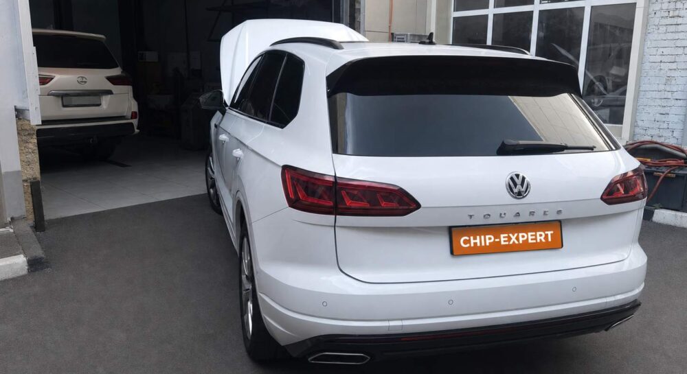 Белый Volkswagen Touareg 3.0TDI 2019 с открытым капотом, вид сзади слева у въезда в ремонтную зону мастерской Чип-Эксперт — chip-expert.pro.